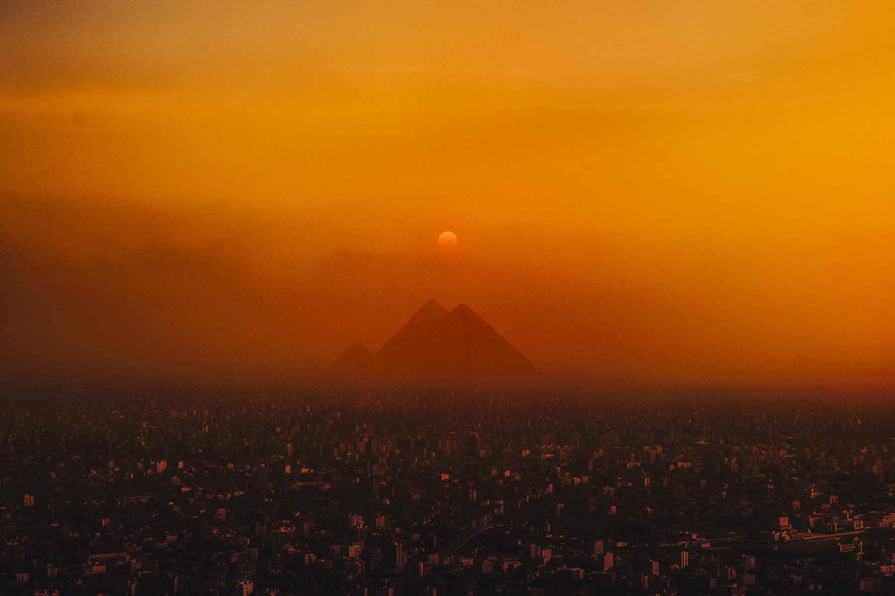 Die Pyramiden von Gizeh über Kairo im orangefarbenen Abendlicht
